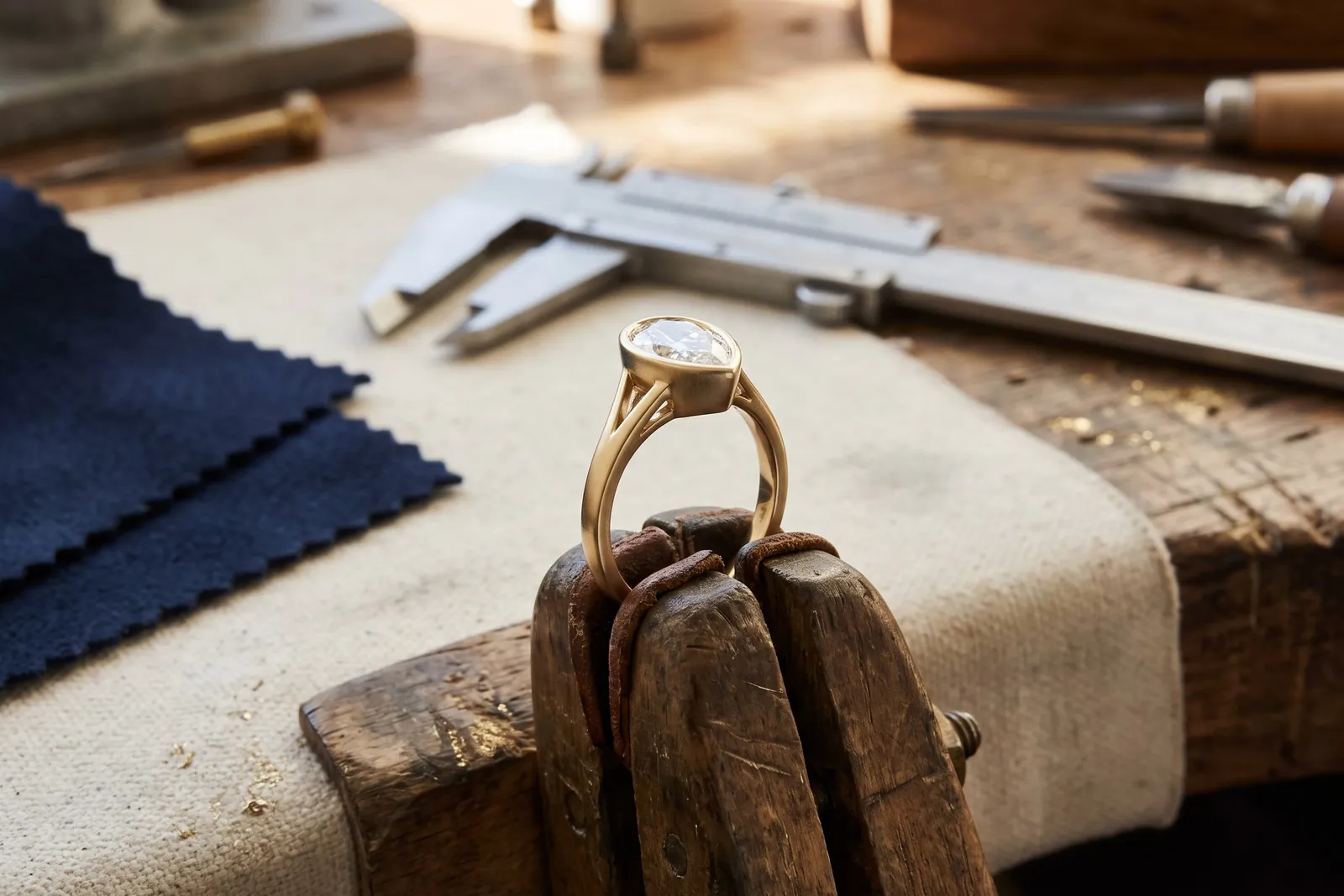 A pear bezel ring held in a jeweler's ring clamp, showing its open gallery and slim, strong shank