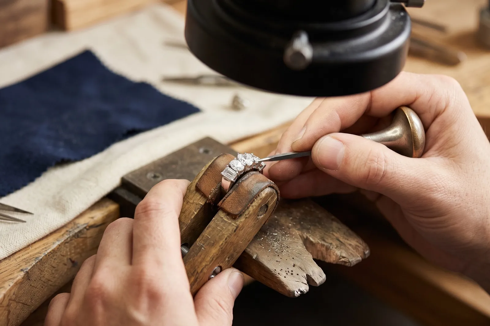 A setter tightening a prong on a diamond ring held in a ring clamp under magnification